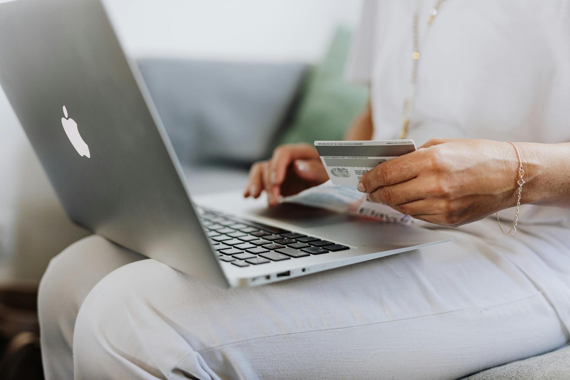 A woman holding a credit card for purchasing something with a laptop on her lap.